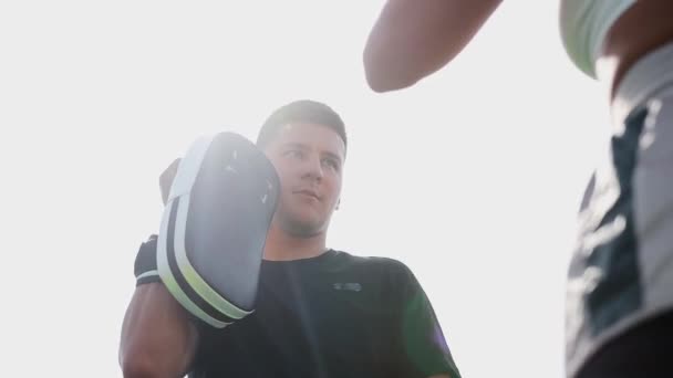 Бокс тренировки на открытом воздухе - молодая женщина в коротких шортах удары в перчатках на руке тренера — стоковое видео