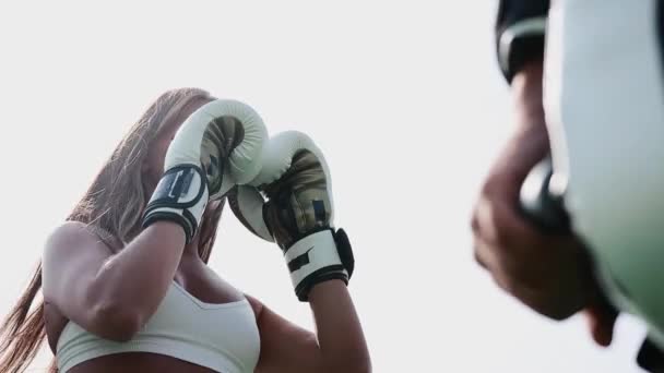 Entrenamiento de boxeo al aire libre - mujer joven en la parte superior blanca perforando en los guantes en su mano de entrenadores — Vídeos de Stock