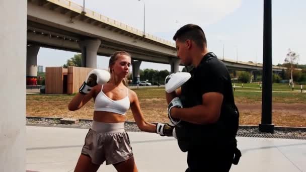 Тренування з боксу - молода жінка з волоссям у хвіст тренування своїх ударів з тренером-чоловіком — стокове відео