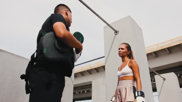 Навчання боксу на будівельному майданчику - молода жінка в боксерських рукавичках тренує своїх ударів з тренером-чоловіком — стокове відео