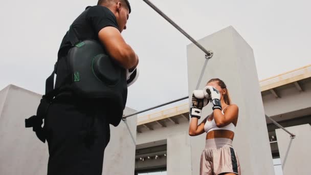 Boxningsträning på byggarbetsplatsen - ung fitnesskvinna i boxerhandskar tränar sina slag med en manlig tränare — Stockvideo