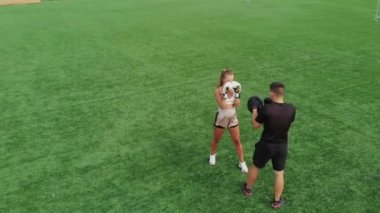 Genç bir kadın, yeşil çimlerde boks antrenmanında, erkek bir koçla.