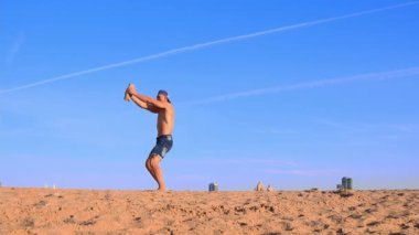 Plajda spor egzersizleri yapan genç bir adam elinde ağır bir taşla oracıkta küçük atlayışlar yapıyor.