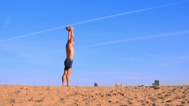 Jonge fitte man doet sport oefeningen op het strand met een zware rots in zijn handen — Stockvideo