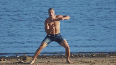 Spor egzersizleri. Genç ve formda bir adam sahilde kaçamak hareketler yapıyor.