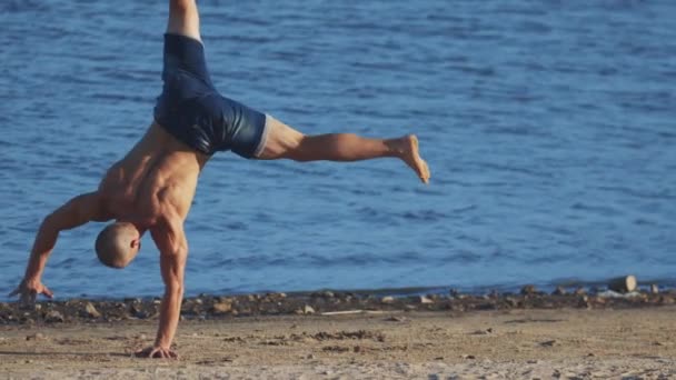 Spor dışarıda egzersiz yapar. Genç ve formda bir adam sahilde perende atar. — Stok video