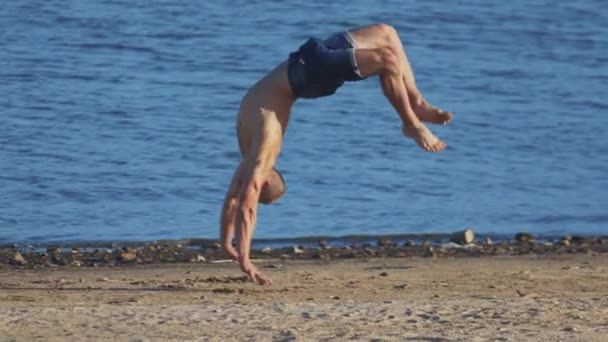Спортивные упражнения на открытом воздухе - молодой человек, выполняющий сальто назад на пляже — стоковое видео