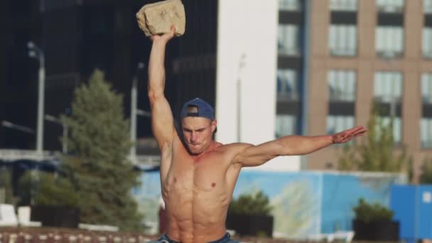 Sportübungen im Freien - junger fitter Mann macht Übungen am Strand - Hocken mit einem Stein in der Hand — Stockvideo