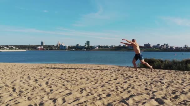 Ung mand løber op og begynder at gøre en række flips på floden kysten – Stock-video