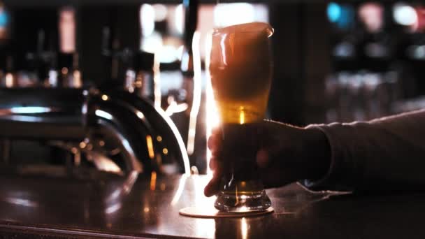 A person puts a glass of draft beer on the stand and foam pours off the border — Stock Video