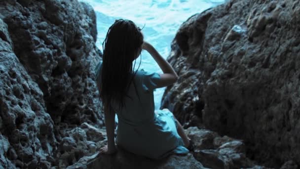 Młoda kobieta z dredami siedząca na skałach przed morzem — Wideo stockowe