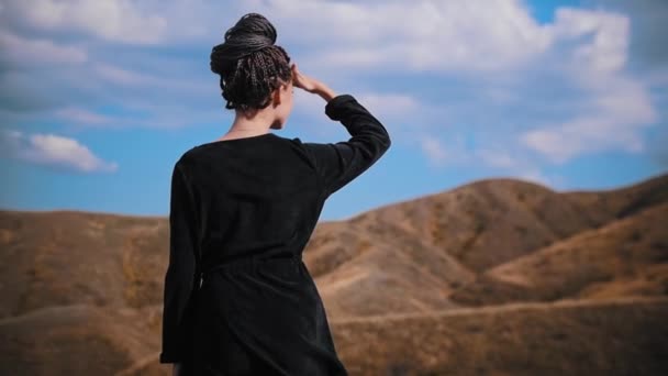 Νεαρή γυναίκα με ράστα να στέκεται στην κορυφή ενός βουνού και να κοιτάζει τριγύρω — Αρχείο Βίντεο