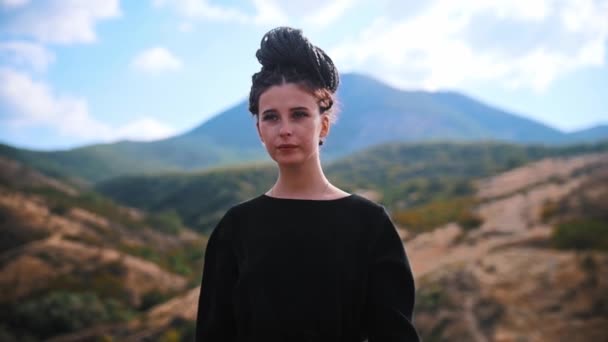 Young beautiful woman with dreadlocks tied up to her head walking on mountain — Stock Video