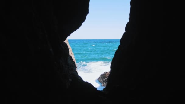 Statisch uitzicht vanuit de donkere grot op de blauwe zee en golven die neerstorten op rotsen — Stockvideo