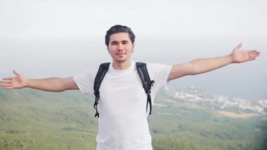 Macera gezisi - mutlu genç adam yürüyüşçüsü dağın tepesinde duruyor ve kameraya bakıyor