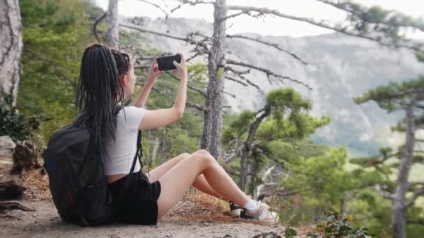 Viaje de aventura - senderista joven con rastas sentadas en el suelo en el bosque y disparando montañas en cámara — Vídeos de Stock