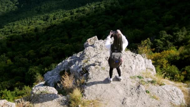 Viaje de aventura - mujer joven excursionista con rastas caminando hasta el borde de una montaña y toma fotos de las fotos y ella misma — Vídeos de Stock