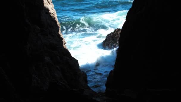Blick von der Höhle auf das blaue Meer und Wellen, die auf Felsen krachen — Stockvideo