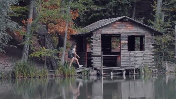 Kisasszony turista sétál a fa kis ház a tó közelében — Stock videók