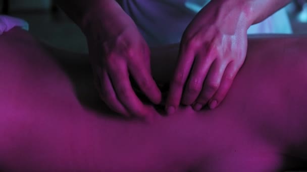 Массаж при неоновом освещении - терапевт массирует кожу на спине своей клиентки — стоковое видео