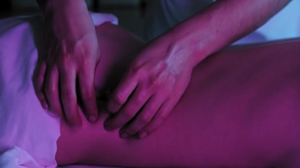 Массаж при неоновом освещении - терапевт массирует мягкую кожу на спине своей клиентки — стоковое видео