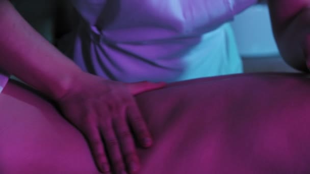 Sesja masażu w neonowym oświetleniu - masaż miękkiej skóry na plecach jej klientki — Wideo stockowe