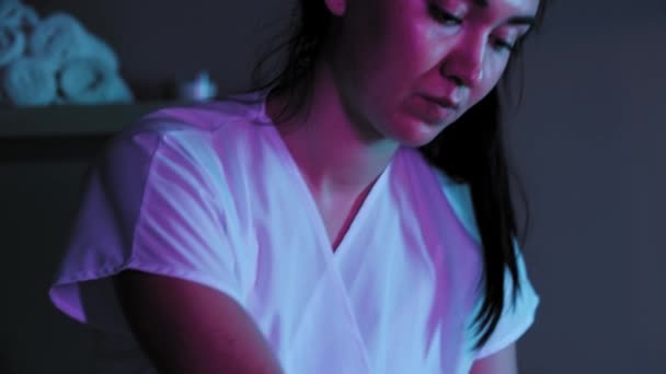Sesión de masaje en iluminación de neón - terapeuta empujando la piel en la parte posterior de su cliente femenino — Vídeo de stock