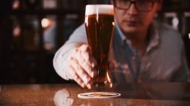 Een man zet een glas bier op de tribune en schuim stroomt van de grens. — Stockvideo