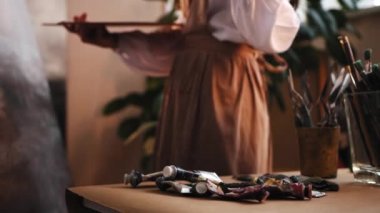 Sanat stüdyosu - genç kadın ressam resim çiziyor - fırça değiştiriyor