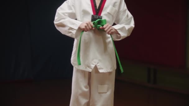 A little boy doing taekwondo - tying up his green belt on the waist — Stock Video