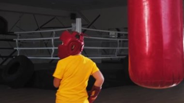 Koruyucu kasklı küçük çocuk, virajdan itibaren kum torbasını tekmeliyor.