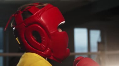 Koruyucu kasklı küçük çocuk boks antrenmanında eldiveniyle yüzüne yumruk yiyor.