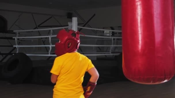 Niño en casco protector pateando el saco de boxeo de la vuelta — Vídeo de stock