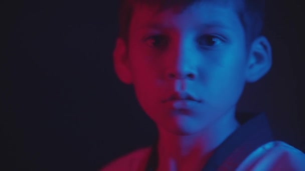 Karanlıkta tekvando yapan küçük bir çocuk neon ışıklarıyla — Stok video