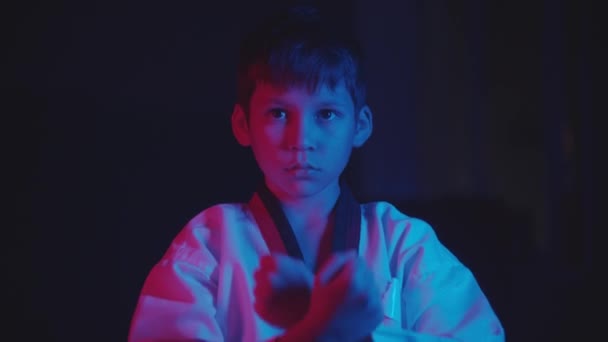 ネオンライトで暗闇の中で武道をしている小さな男の子 – 立っている位置 — ストック動画