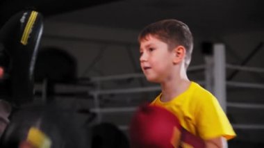 Küçük gülümseyen çocuk boks yapıyor. Koçunun eline tampona vuruyor.