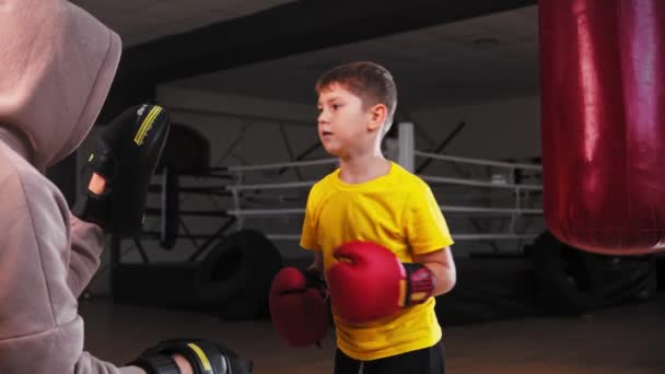 Маленький улыбающийся возбужденный мальчик, занимающийся боксом - ударяя по подушечкам на руках своего тренера и уклоняясь от контратаки — стоковое видео