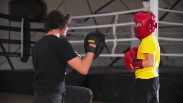 Маленький усміхнений хлопчик в захисному шоломі робить бокс з молодим тренером — стокове відео