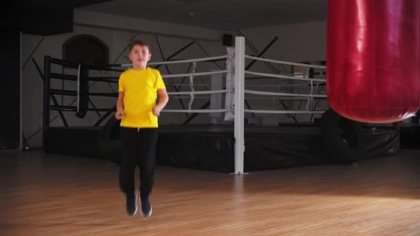 Un niño sonriente tratando de saltar sobre la cuerda cerca del ring de boxeo — Vídeos de Stock