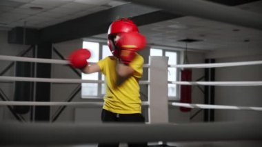 Boks eldivenli, kafasında kaskla dövüşen küçük bir çocuk.