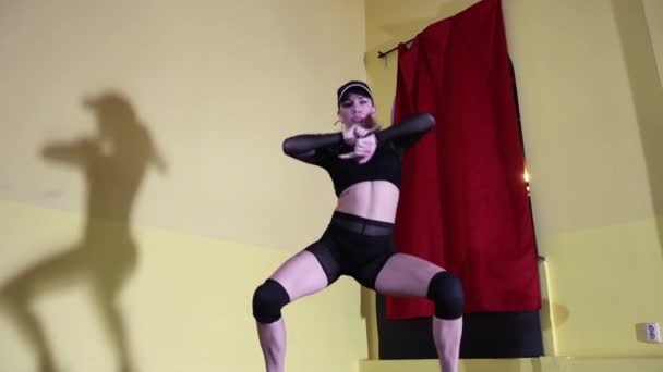 Блондинка с татуировкой сексуальная танцовщица в полупрозрачном костюме и танцующая в шапочке в жёлтой студии — стоковое видео