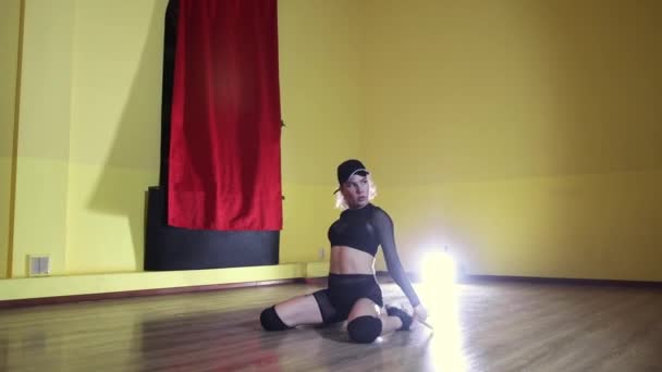 Szőke felnőtt tetovált rugalmas nő fekete áttetsző öltönyben és sapka tánc sárga stúdióban — Stock videók