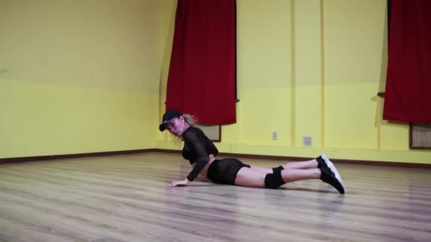 Loira tatuado mulher flexível dançarina profissional em terno preto translúcido e um boné realizando uma dança em estúdio amarelo — Vídeo de Stock