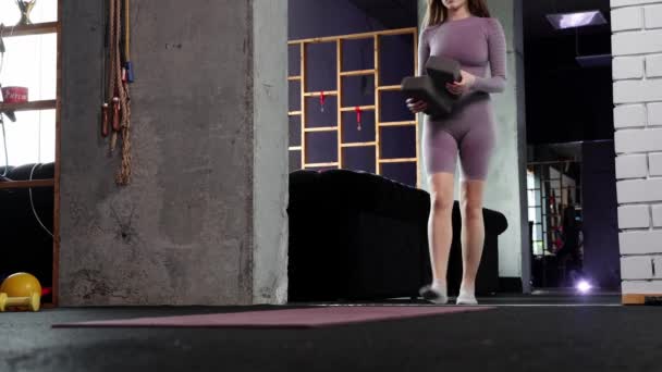 Junge Frau macht Pilates - bringt zwei zusätzliche Geräte für den Unterricht mit und sitzt auf dem Spagat — Stockvideo
