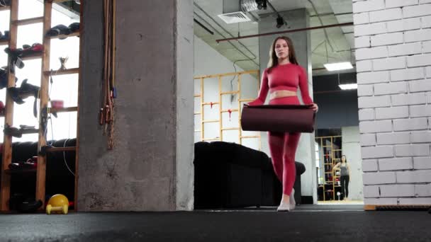 Mujer joven haciendo pilates - trae en el gimnasio una esterilla de yoga y se acuesta en ella — Vídeos de Stock