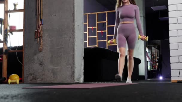 Ung kvinna gör pilates - tar in gymmet två små hantlar och sätter håret i hästsvans — Stockvideo