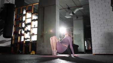 Genç bir kadın pilates egzersizi yapıyor. Yoga minderinde oturarak ayak parmaklarını ısıtıyor.