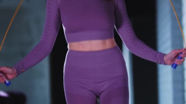 Joven mujer bonita en traje deportivo púrpura saltando sobre la cuerda de salto en el gimnasio — Vídeos de Stock