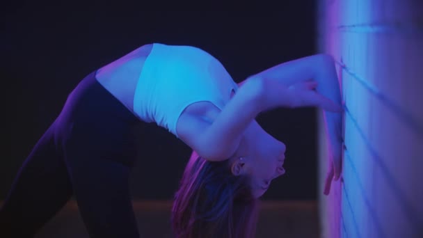 Giovane donna che si esercita in illuminazione al neon piega il corpo appoggiato con le mani contro il muro — Video Stock