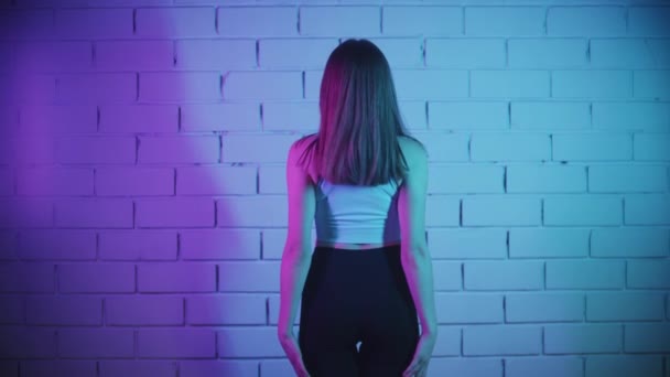 Улыбающаяся молодая женщина, занимающаяся фитнесом в неоновом освещении на фоне кирпичной стены - наклоняется назад — стоковое видео